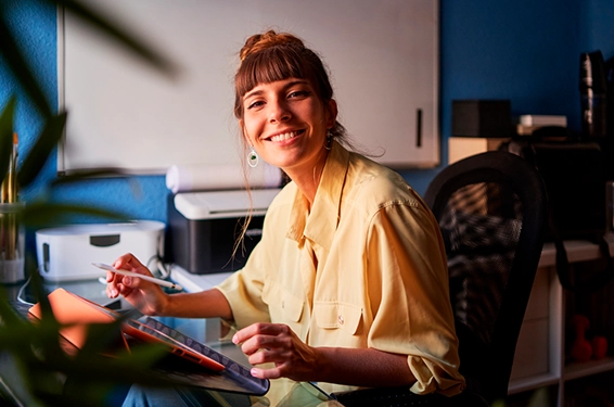 A graphic designer working from home with her digital tablet looking at the camera and smiling